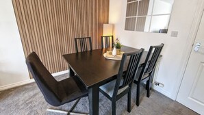 Un comedor con una mesa de madera oscura y sillas negras, una lámpara y un jarrón decorativo sobre la mesa.