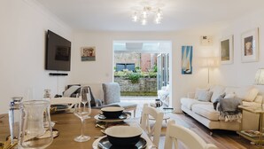 A dining area with a table set for four, a sofa, and a TV mounted on the wall. - Stylish Retreat with Garden in Tetbury (Tetbury)