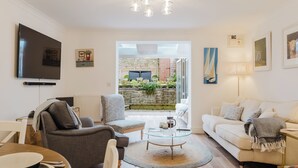 A modern living room with a flat-screen TV, a sofa, a coffee table, and a dining area. - Stylish Retreat with Garden in Tetbury (Tetbury)