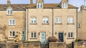 A row of stone houses with multiple windows and doors, some with shutters, and a small garden area with a potted plant. - Stylish Retreat with Garden in Tetbury (Tetbury)