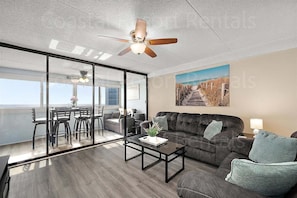 A modern living room with a sofa, coffee table, and a dining area with chairs and a table. - 2 Bedroom Condo with Outdoor Pool and Beautiful Ocean Views! (Ocean City)