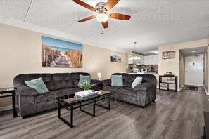 A living room with two dark sofas, a coffee table, and a ceiling fan.