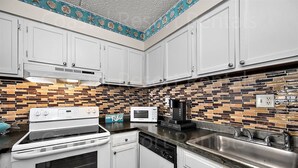 A kitchen with white cabinets, a stove, a microwave, and a coffee maker. - 2 Bedroom Condo with Outdoor Pool and Beautiful Ocean Views! (Ocean City)