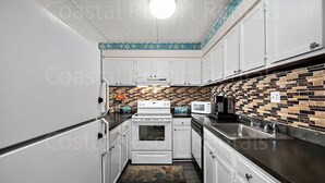 A compact kitchen with white cabinets, a tiled backsplash, and a central stove. - 2 Bedroom Condo with Outdoor Pool and Beautiful Ocean Views! (Ocean City)