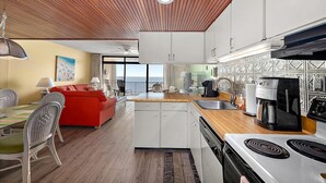 A modern kitchen with a wooden ceiling, white cabinets, a built-in stove, and a view to the outside. - HPN-1 Bedroom Oceanfront Condo, Steps to the Beach! (Ocean City)