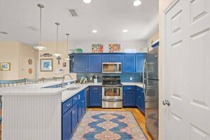 Une cuisine avec des meubles de couleur bleue, un îlot central, des appareils électroménagers en acier inoxydable et un tapis aux couleurs vives.