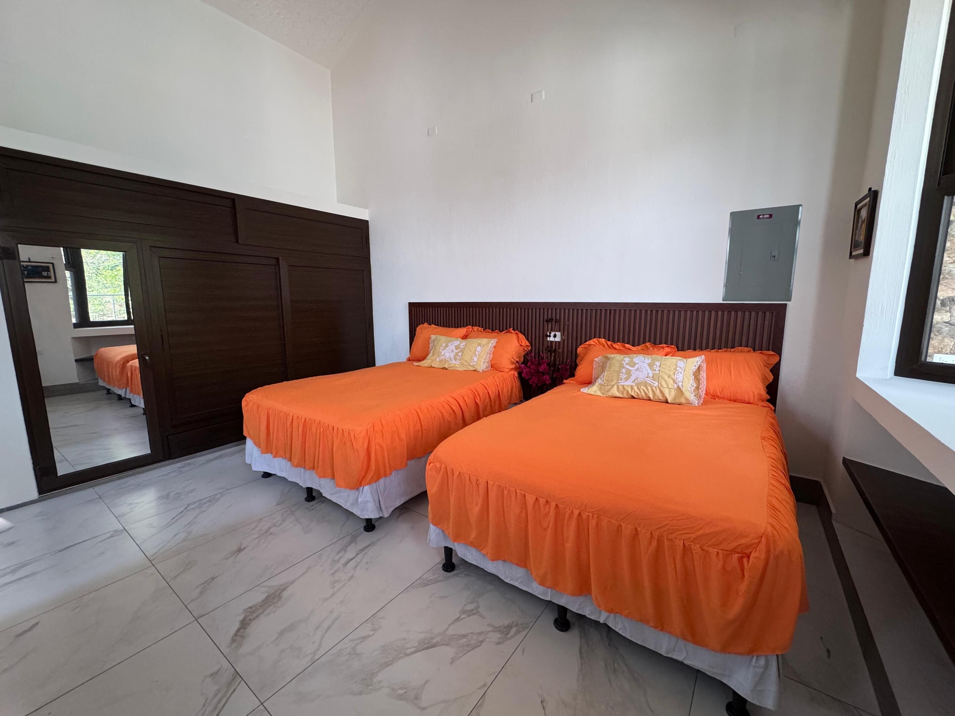 A hotel room with two beds, a large mirror, a wardrobe, and a window.