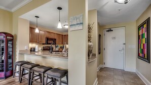 A kitchen with wooden cabinets, a central island with stools, pendant lighting, and a door with a calendar. - ✨Water Views | Great Amenities | AAA Four Diamond Resort | The Marina 4-406✨ (Myrtle Beach)