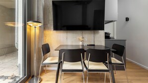 A modern dining area with a large table, four chairs, a floor lamp, and a flat-screen TV mounted on the wall. - Global Living I The Graf (Berlin)