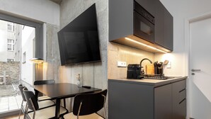 A modern kitchen with a flat-screen TV mounted on the wall, a dining area with a table and chairs, and a view of the outside through a large window. - Global Living I The Graf (Berlin)