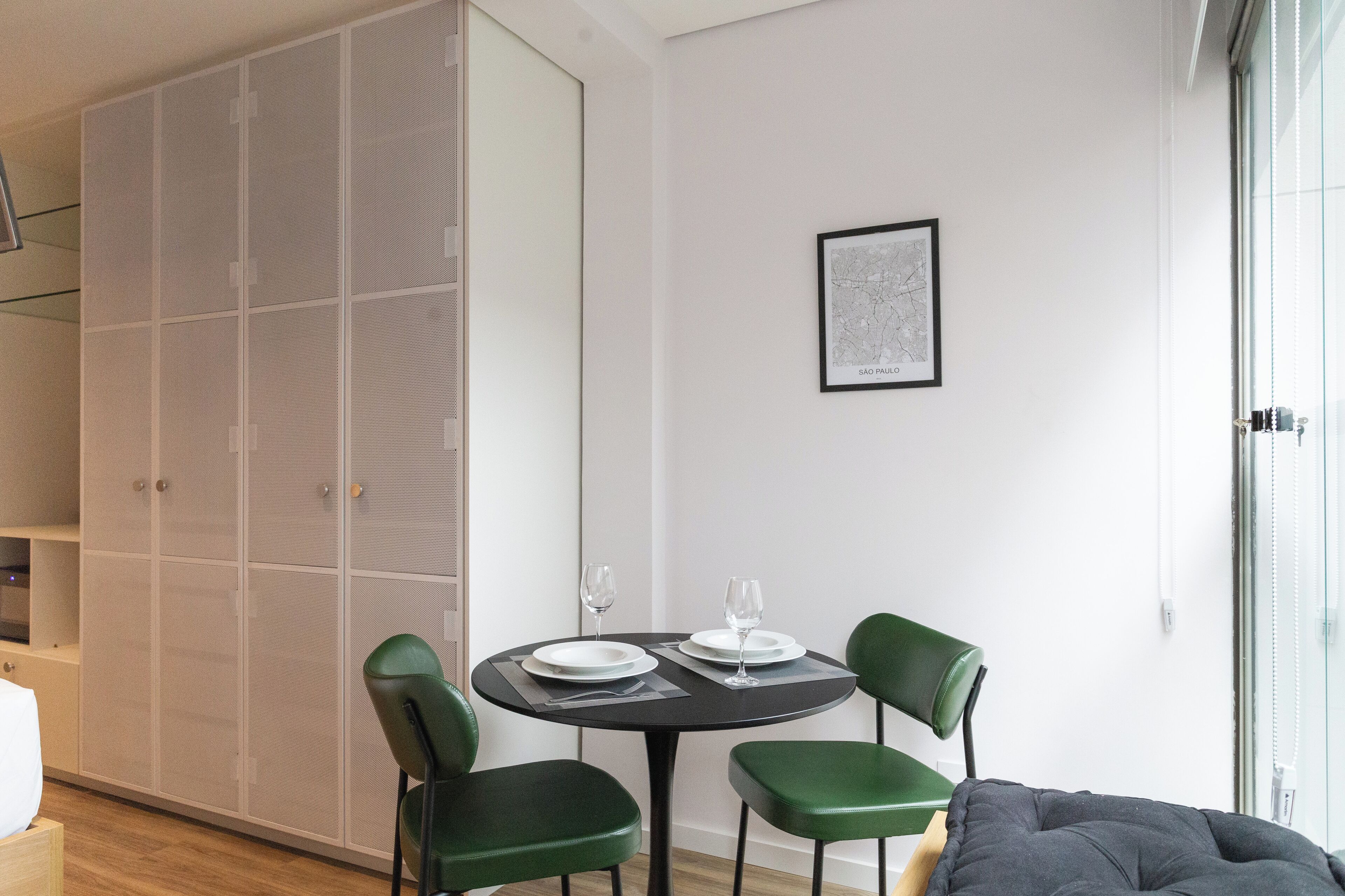 Ein modernes Zimmer mit einem runden Esstisch für zwei Personen, grünen Stühlen, einem grauen Sofa und einem großen Kleiderschrank.