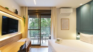 Una habitación de hotel moderna con una cama grande, un televisor de pantalla plana montado en la pared, un balcón con mesa y sillas, y un equipo de aire acondicionado en la pared.