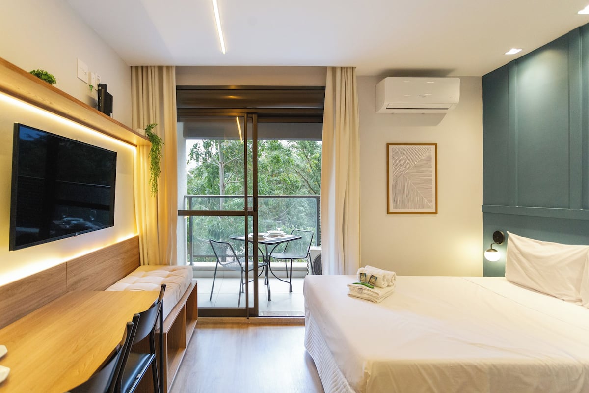 Een moderne hotelkamer met een groot bed, een flatscreen televisie aan de muur, een balkon met een tafel en stoelen, en een airconditioningunit.