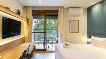 Una habitación de hotel moderna con una cama grande, un televisor de pantalla plana montado en la pared, un balcón con mesa y sillas, y un equipo de aire acondicionado en la pared.