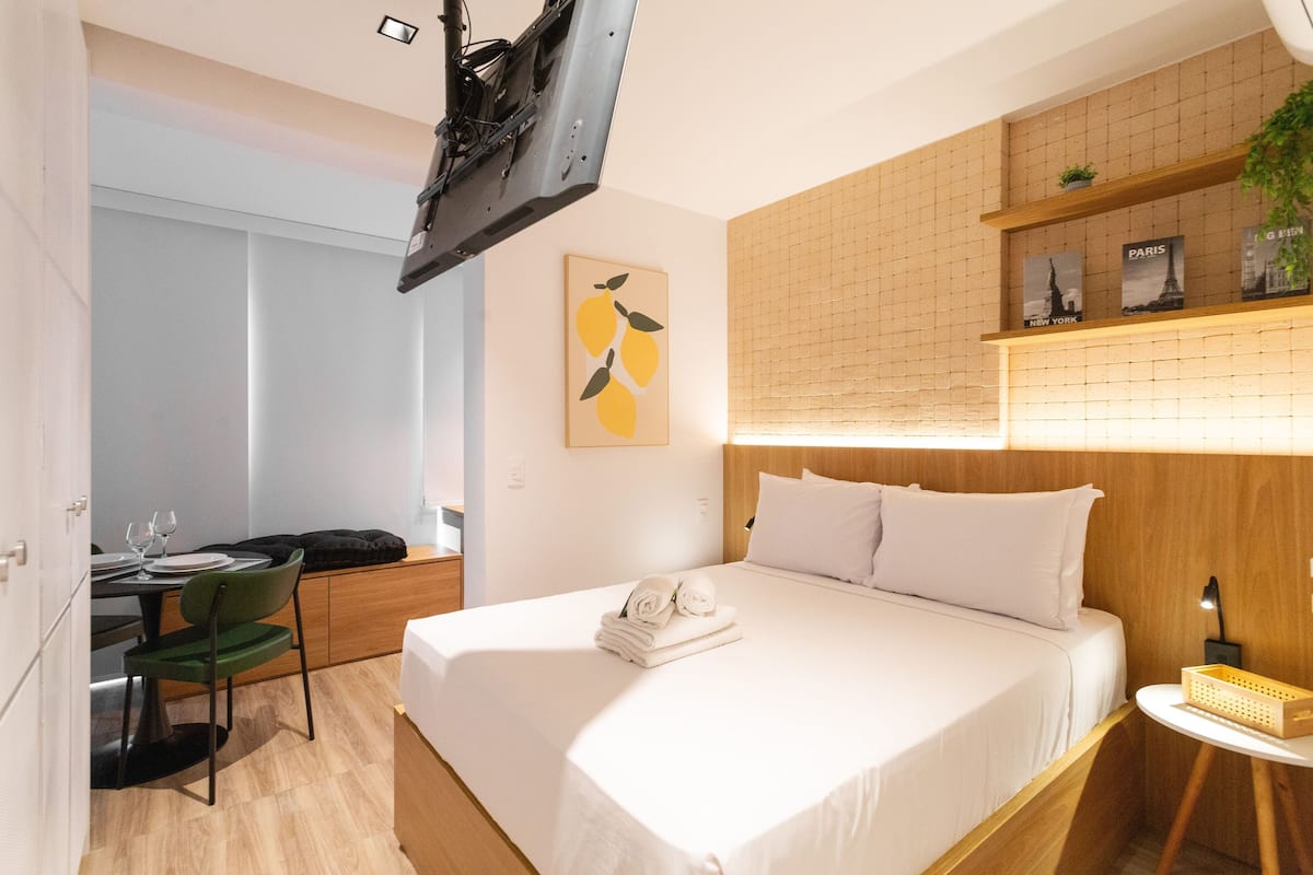 Een moderne hotelkamer met een groot bed, een bureau met stoel, een aan de muur bevestigde televisie en een kleine plant op een plank.