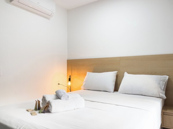 Una camera d'albergo con un letto, cuscini, un comodino, una lampada e un condizionatore d'aria.