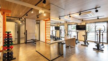 Un gimnasio moderno con equipo de ejercicio, un muro de espejos y amplias ventanas.