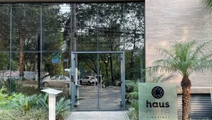 La entrada a un edificio con puerta de vidrio, un letrero que dice 'haus mitre pinheiros' y una palmera a la derecha.