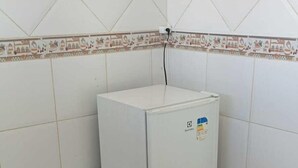 Ein kleiner, weißer Kühlschrank steht in einer Ecke des Raumes mit weißen Fliesenwänden und -boden.