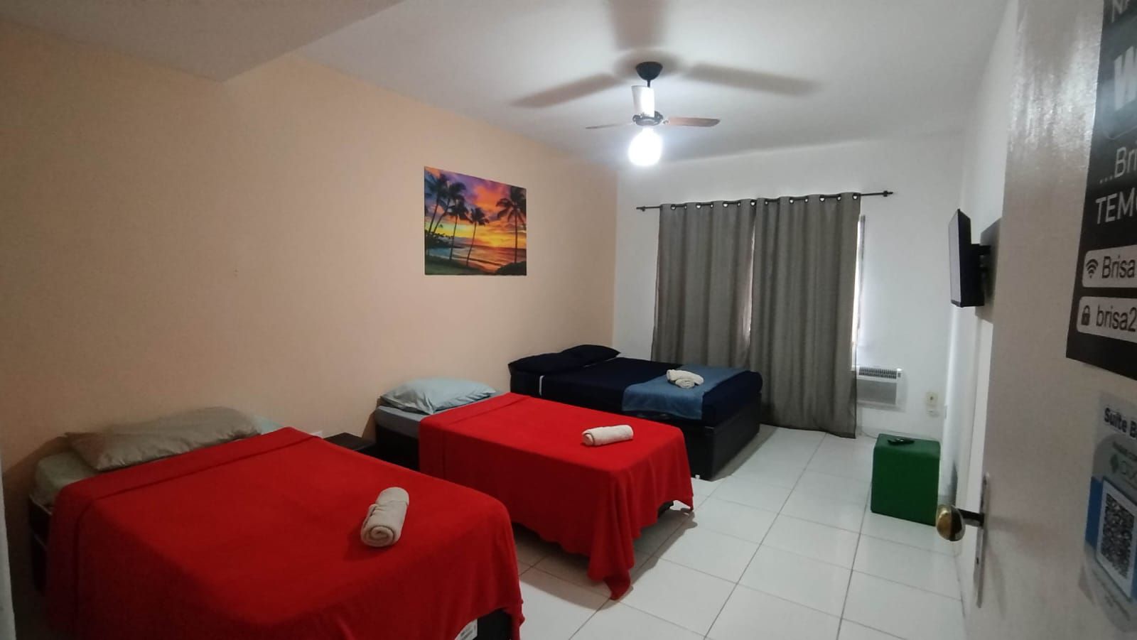 Una habitación con dos camas, un ventilador de techo, un cuadro y una ventana con cortinas.