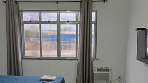 Una habitación con dos camas, una ventana con cortinas, un radiador y un ventilador de techo.