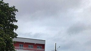Un edificio con fachada roja y blanca, varios coches aparcados y un área verde al frente.