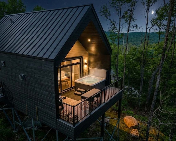 Una cabaña con jacuzzi, balcón y vista al bosque.