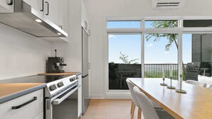 A modern kitchen with a built-in oven, a coffee machine, and a dining area with a wooden table and chairs. - Spa | Mountain | Modern Comfort | Elska (Saint-Côme)