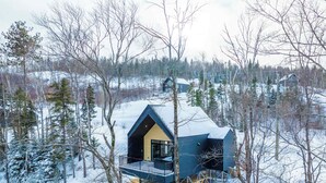 A cabin with a balcony, surrounded by snow-covered trees and a forested landscape. - Spa | Mountain | Modern Comfort | Elska (Saint-Côme)