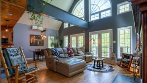 A spacious living room with a leather sofa, a rocking chair, and a dining area with a table and chairs.