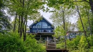 A large, dark blue cabin with a prominent central window and a wooden deck leading to a second-story balcony.