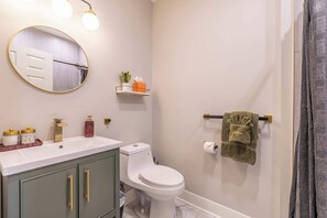 Ein Badezimmer mit Toilette in Weiß, einem Waschbecken mit goldfarbenen Armaturen, einem Spiegel mit goldener Rahmung und einem Handtuchhalter mit Handtuch.