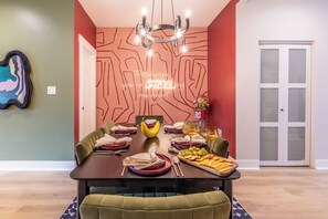 A dining room with a table set for four, a fruit bowl, and a wall with a geometric pattern.