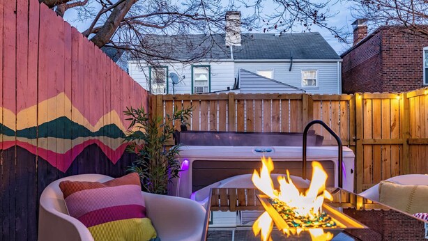 Un jardin avec un foyer, une chaise blanche, un mur aux couleurs vives et une clôture en bois.