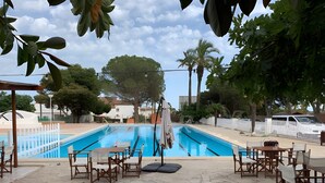An outdoor swimming pool with lounge chairs and tables, surrounded by trees and a white fence. - Holiday Home 'Deltabahia' with Shared Pool, Wi-Fi and Air Conditioning (Alcanar)