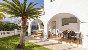 A white building with a covered patio, outdoor seating, and a palm tree. - Holiday Home 'Deltabahia' with Shared Pool, Wi-Fi and Air Conditioning (Alcanar)