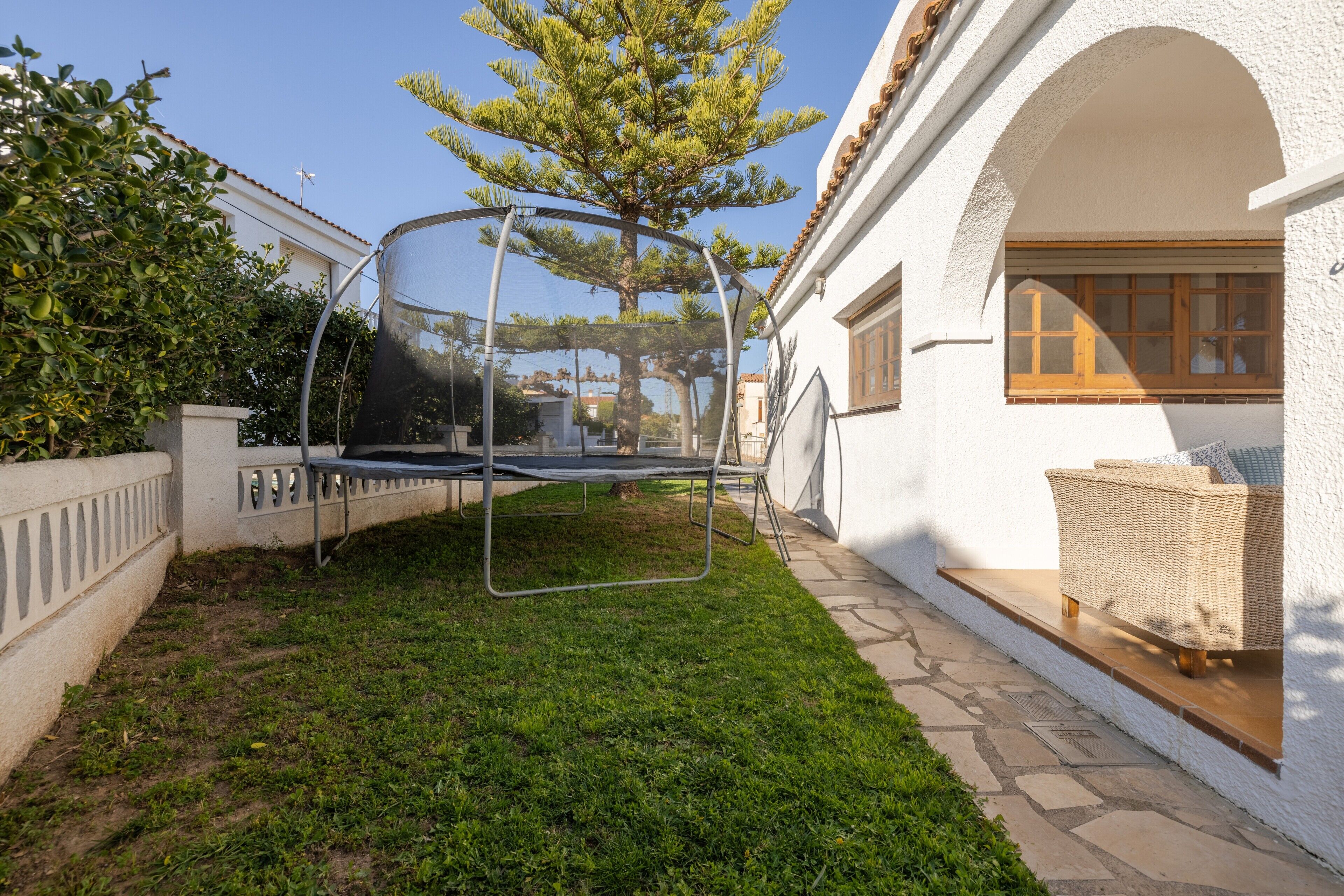 Un edificio blanco con un trampolín cubierto, una silla de mimbre y un árbol.