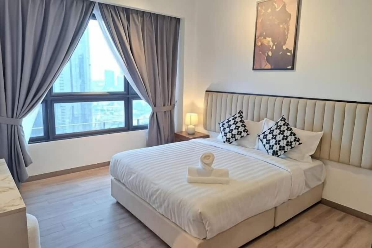 A hotel room with a large bed, a nightstand, a window with curtains, and a city view.