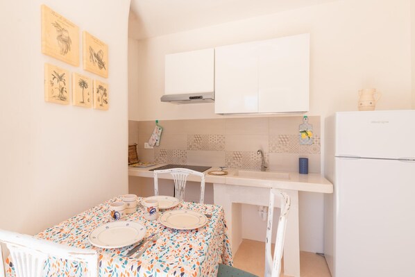 A small kitchen with white cabinets, a white refrigerator, and a dining table with plates and cups.
