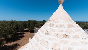 A white stone structure with a pointed top, surrounded by olive trees and a clear blue sky. - Trullo Calamo tra Mare e Citt (Ostuni)
