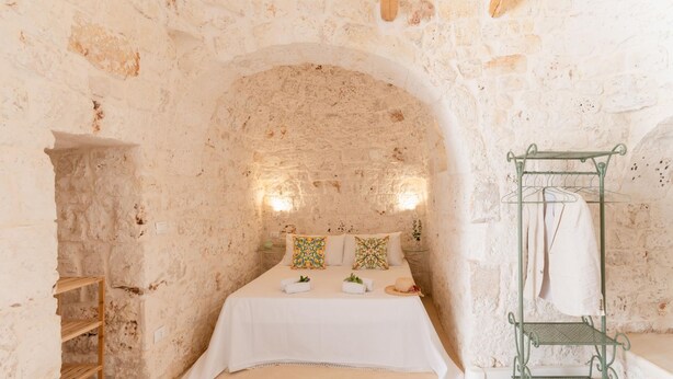 A stone-walled room with a bed, a wooden shelf, and a metal drying rack. - Trullo Calamo tra Mare e Citt (Ostuni)