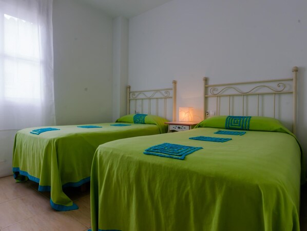 Two single beds with green bedding and blue accents, a bedside table with a lamp, and a window with sheer curtains. - Rotonda I 88 in Conil de la Frontera (Conil de la Frontera)