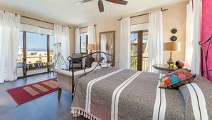 A spacious bedroom with a large bed, a ceiling fan, and a balcony with a view.
