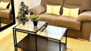 A modern living room with a brown sofa, a glass coffee table, a potted plant, and a large mirror. - Modern apartment in Juan de Austria (Málaga)