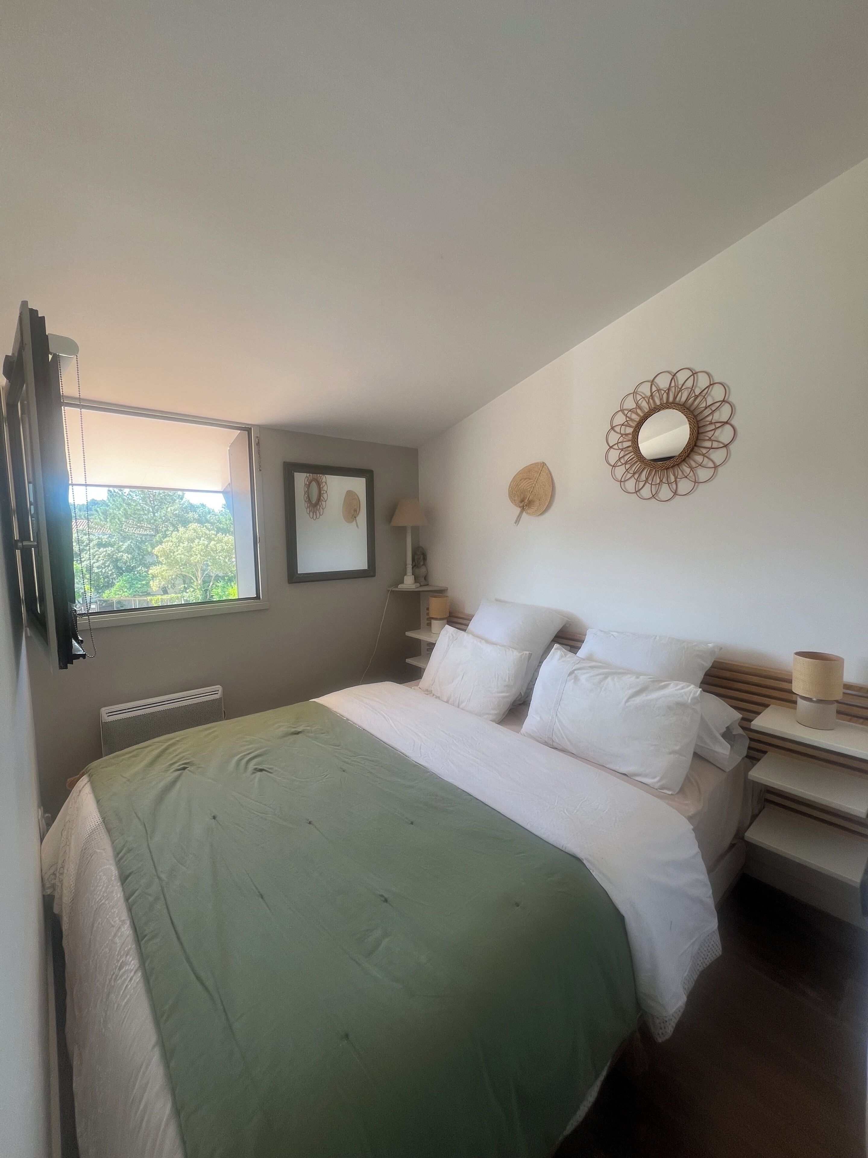 Ein Schlafzimmer mit Bett, Nachttischen, einer Lampe, einer Wanddekoration und einem Fenster.
