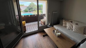A room with a sliding glass door leading to a balcony with a pool. There is a sofa and a wooden table with candles.