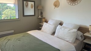 A bedroom with a bed, pillows, a bedside lamp, a wall-mounted mirror, and a framed artwork.