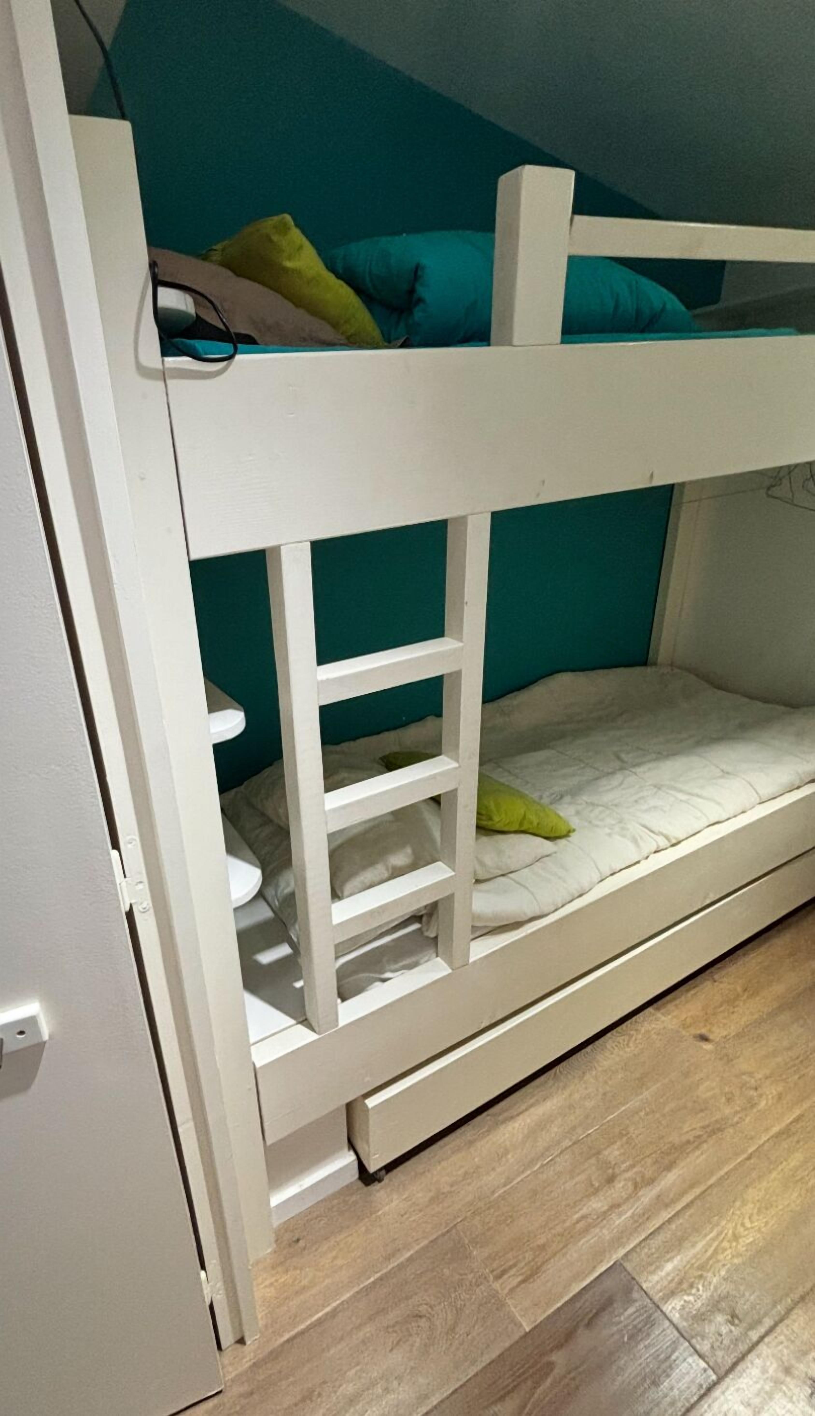 A bunk bed with a ladder, a white mattress, and a teal wall in the background.
