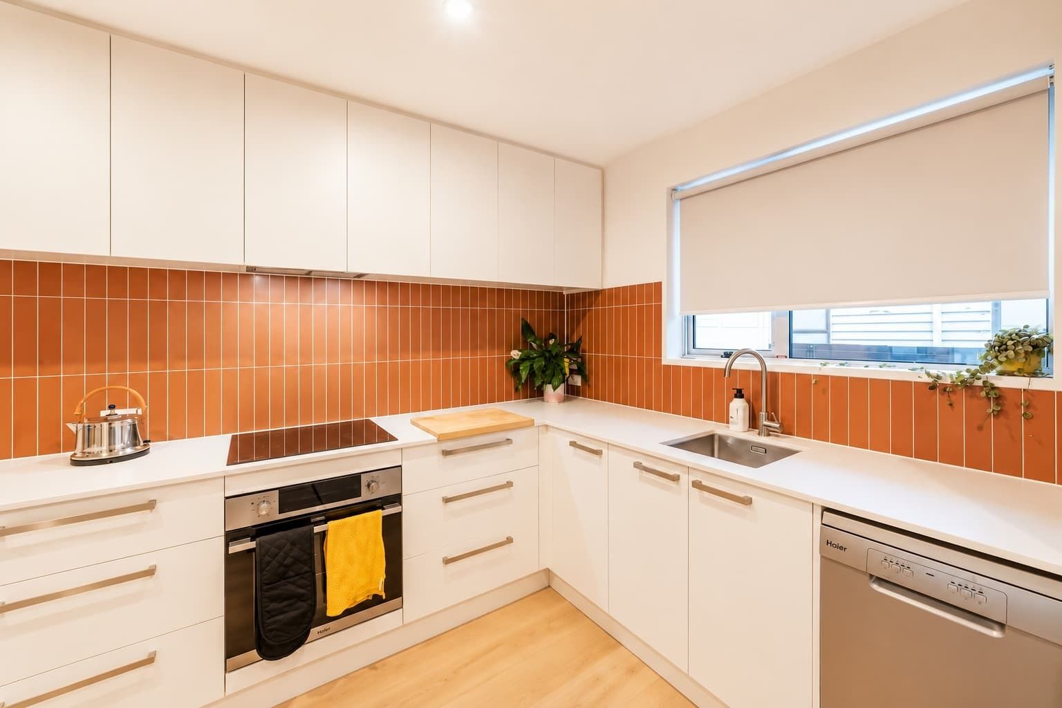 A modern kitchen with white cabinets, a stainless steel sink, and a built-in oven.