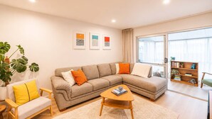 Una sala moderna con un sofá seccional beige, una mesita de centro de madera, un sillón amarillo y una estantería.